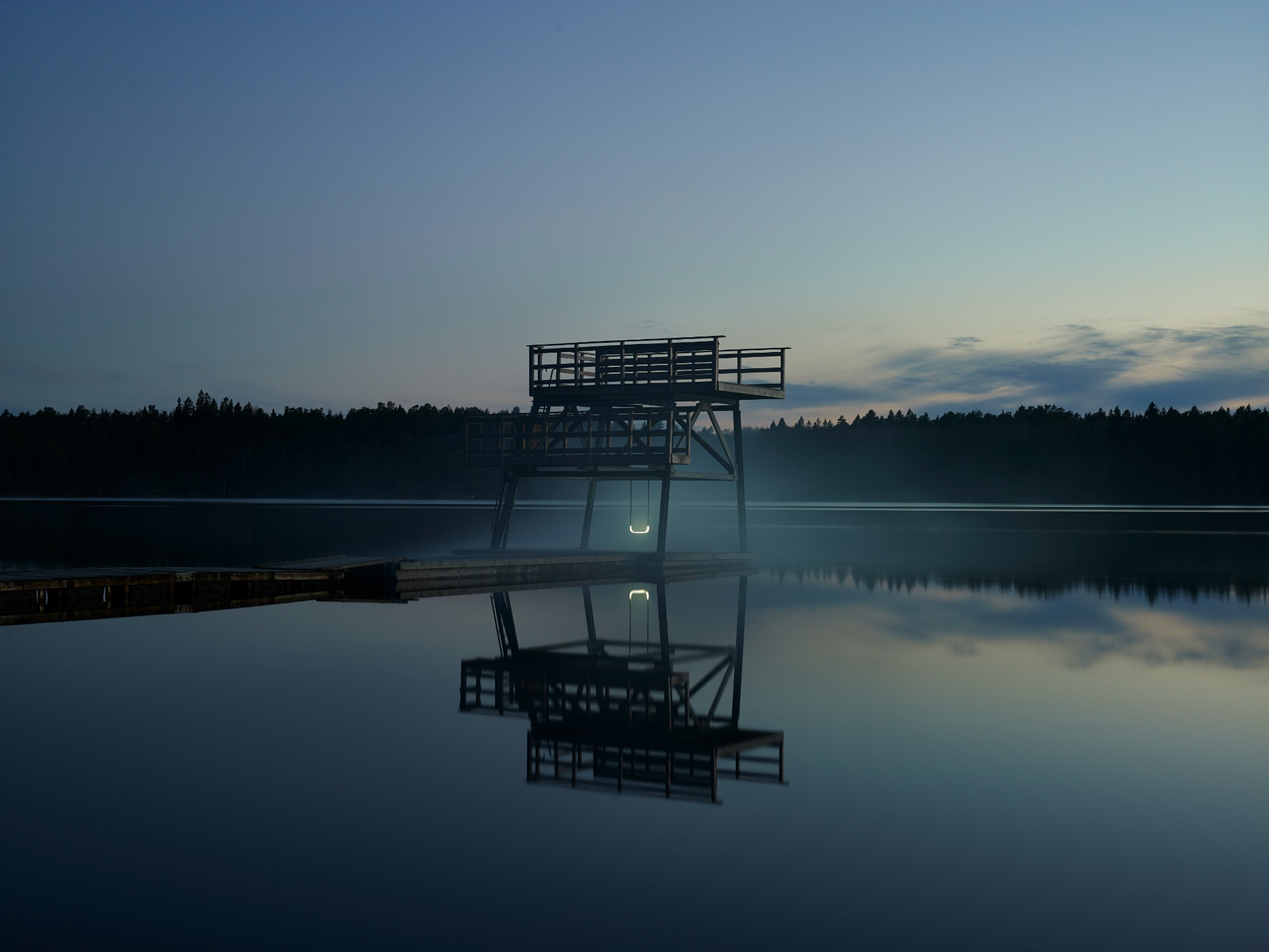 Sense Lightswing lyser under et stupetårn ved et stille vann i skumringen